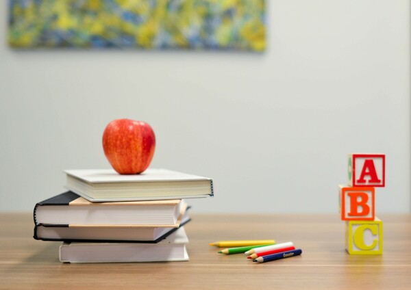 3 books stacked with an apple on top, pencil crayon and ABC letter blocks sit on a table.